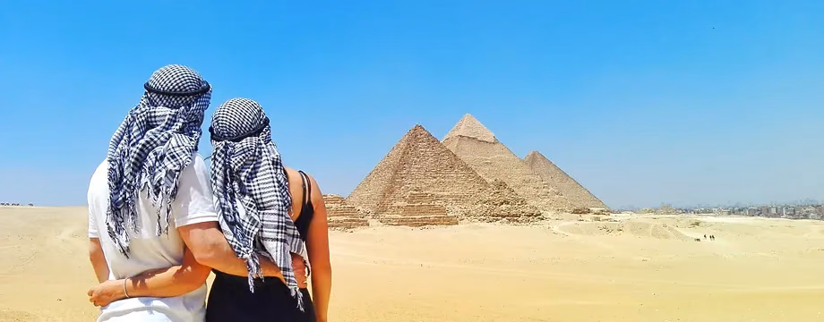 Two guests in keffiyehs looking out at the pyramids from the dunes